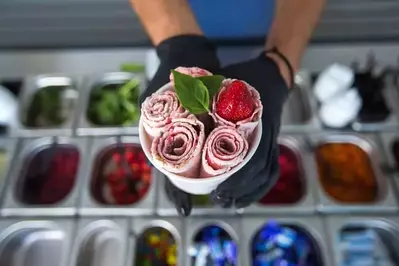 a person holding strawberry rolled ice cream in a cup