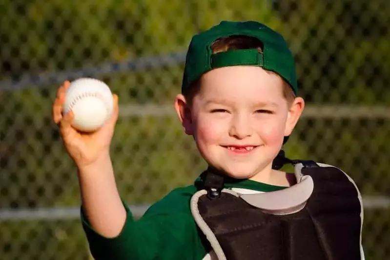 young boy in catchers gear holding baseball