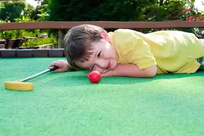 young boy plays miniature golf lines up golf ball