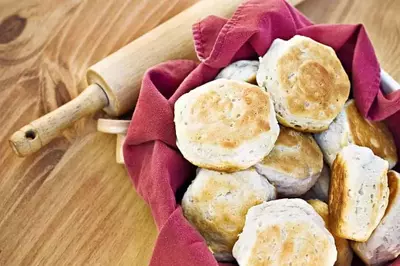 A basket of freshly baked biscuits next to a rolling pin.