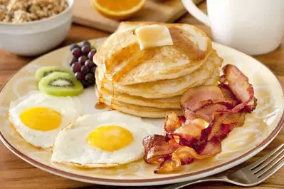 A plate of delicious pancakes, eggs, bacon, and fruit.